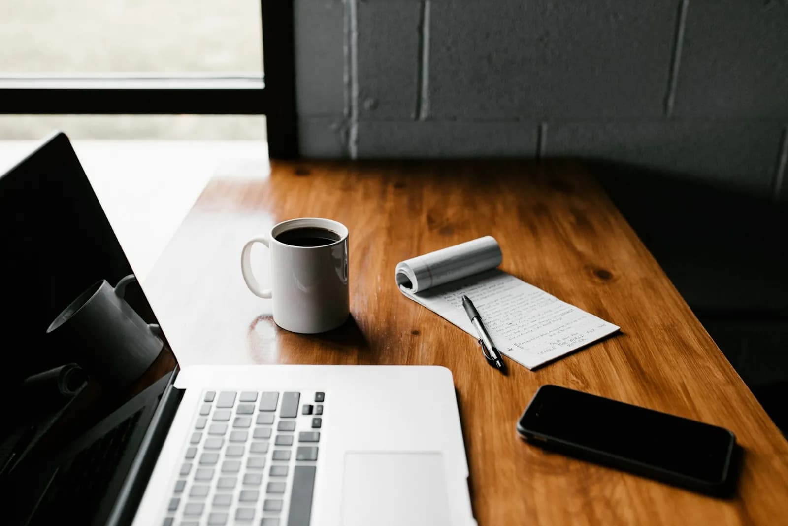 A laptop, a notebook and a coffee on a work desk